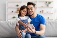 Smiling Dad And Daughter Sitting On Couch, Using Phone