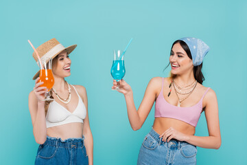 Wall Mural - Positive friends in tops and necklaces holding cocktails isolated on blue.