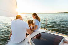 Rear-View Of Family Sailing On Yacht Sitting Together On Deck