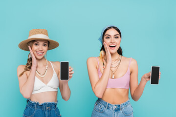 Sticker - Positive women in tops holding smartphones isolated on blue.