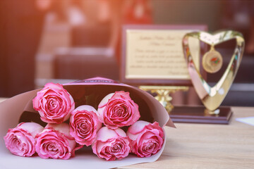 Wall Mural - Bouquet of flowers from roses on a blurred background of a gold medal. Graduation day. Toned background