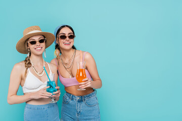 Canvas Print - Smiling women in sunglasses holding cocktails isolated on blue.