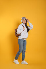 Poster - Beautiful young woman with stylish leather backpack and headphones on yellow background