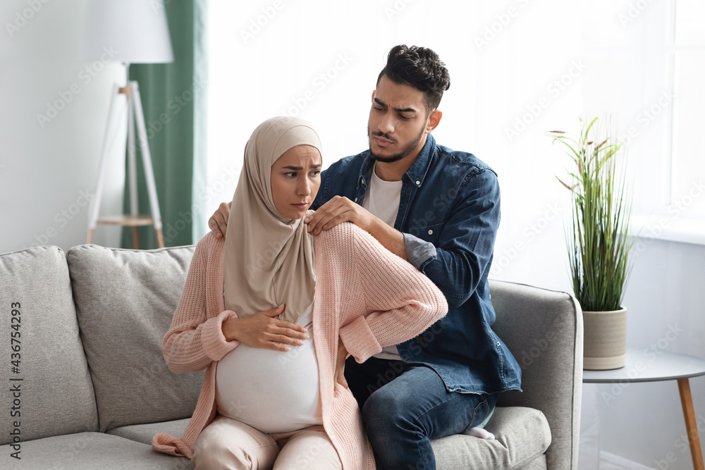 Caring arab husband making neck massage to pregnant muslim wife at home - obrazy, fototapety, plakaty 