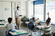 © Seventyfour - Wide angle portrait of male African-American teacher wearing mask in school classroom, covid safety measures, copy space