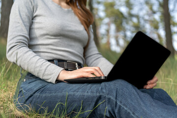 Poster - Girl holding a laptop on her lap is working outdoors