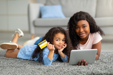 Wall Mural - Online shopping from home. Positive black lady and her daughter using credit card and tablet pc to buy things on web