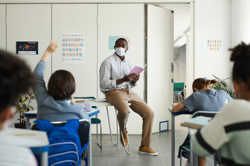 Wall Mural - Wide angle portrait of African-American teacher wearing mask in school classroom, covid safety measures, copy space