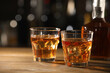 © New Africa - Glasses of whiskey with ice on wooden table in bar, space for text