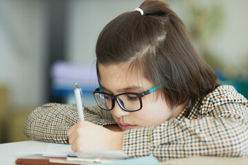 Close up portrait of cute boy wearing glasses sitting at desk in school classroom and writing