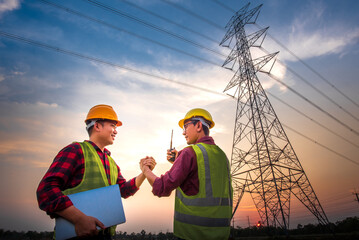 two asian men with electrical engineers standing at the power station standing in the air shaking ha