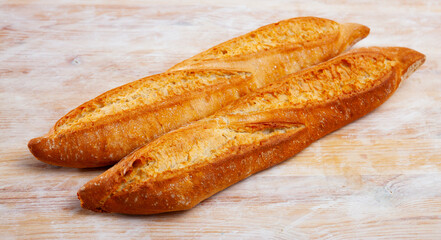 Closeup of two long thin French loaves on wooden surface. Fresh baked goods