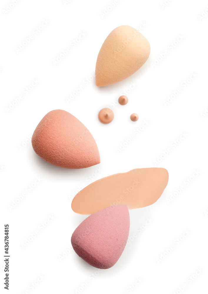 Makeup sponges with samples of tonal foundation on white background