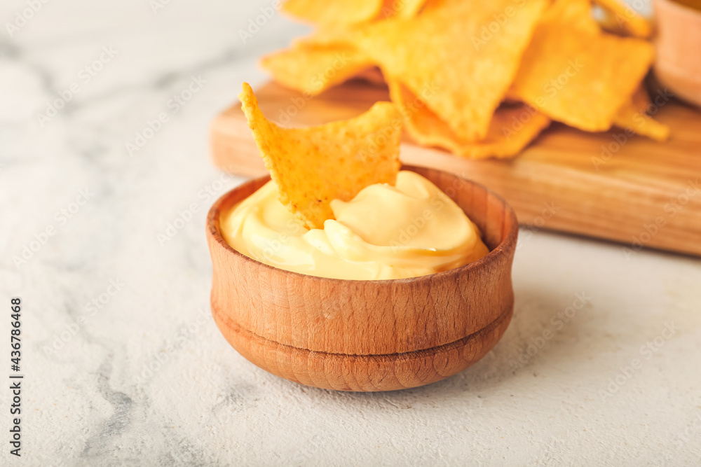 Board with tasty nachos and sauce on light background, closeup