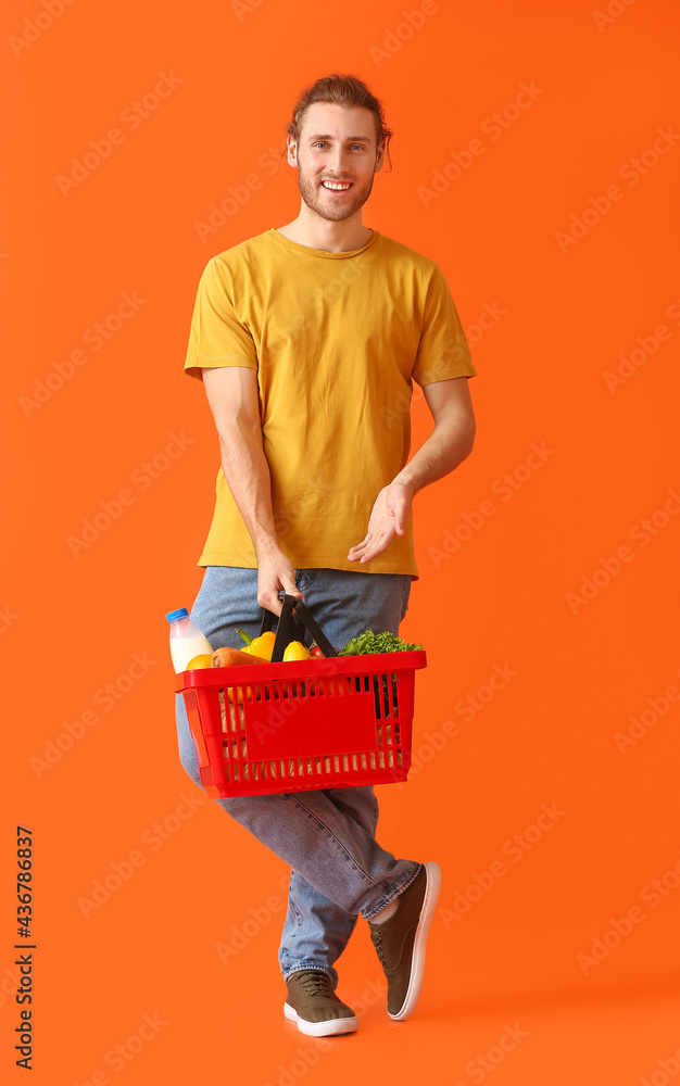 Young man with shopping basket on color background