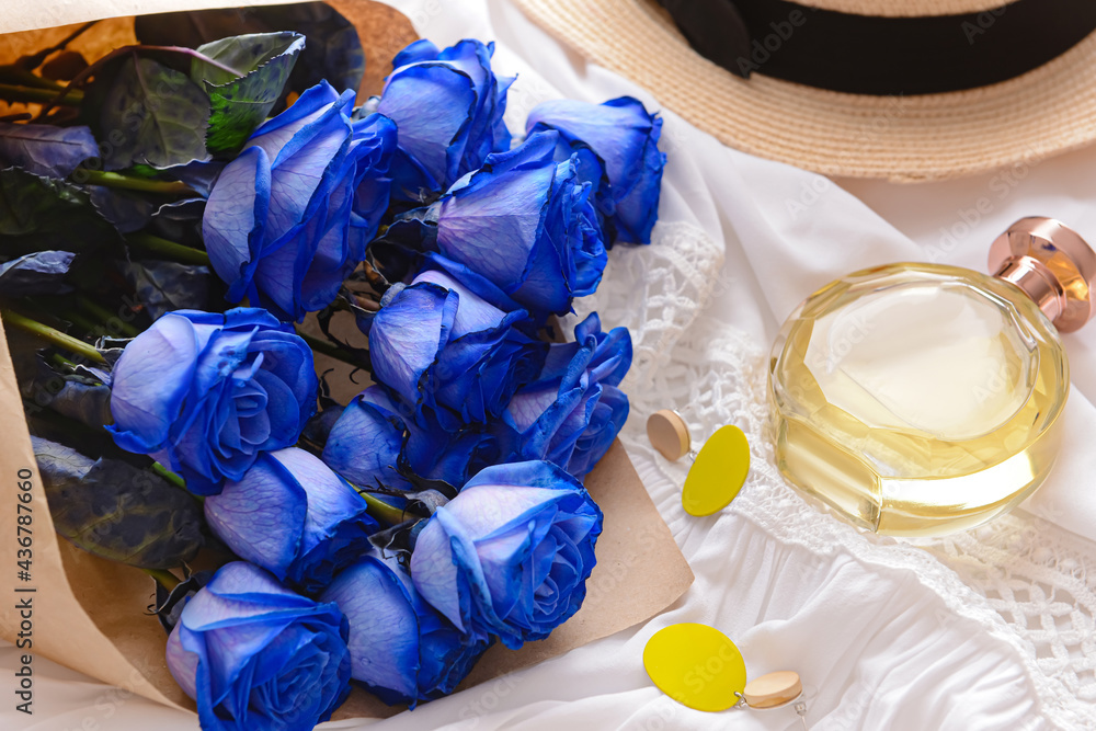 Beautiful blue roses, earrings and perfume on light background