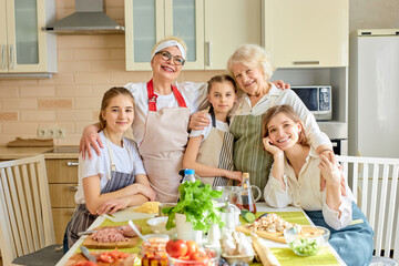 Wall Mural - Portrait Of Sweet Pretty Different Generation Family, Females At Day time in kitchen At Home. Good-lookign Senior Ladies Hugging Children, Teaching To Cook, Having Fun Together, Copy Space