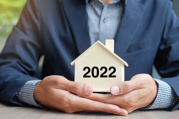 Sticker - Businessman hands holding wooden House model with 2022 New Year text. Property insurance and real estate concepts