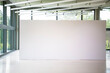Modern gallery interior with blank white empty canvas. Contemporary, open space, city view and daylight. Marble floor. Green trees in background. Light spots,generic design furniture and building.