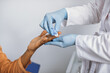 Close up cropped photo of hands of a female lab worker in white coat and gloves, taking a patient's blood sample, using painless scarifier. Black woman patient ready to blood test