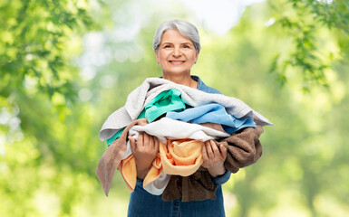 Poster - cleaning, laundry and old people concept - portrait of smiling senior woman in denim shirt with heap of bath towels over green natural background