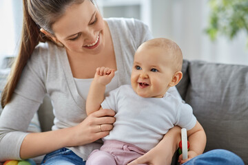 Wall Mural - family, motherhood and people concept - happy smiling mother and little baby playing with rattle at home