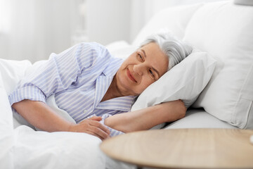 Poster - old age and people concept - happy smiling senior woman lying in bed at home bedroom