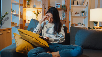 Thoughtful Asia lady holding phone feeling sad waiting for call sit at sofa in living room at house night feel lonely, Sad depressed teenager spend time alone, Social distance, Coronavirus quarantine.