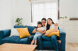 © tirachard - Happy Asian family enjoy their free time relax together at home. Lifestyle Korean dad, mom and daughter watching TV together and having fun lying on sofa in living room in modern house.