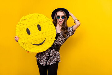 Portrait of attractive amazed cheerful girl holding in hands emoticon wow reaction isolated over bright yellow color background