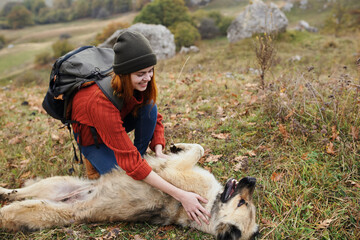 woman hiker with backpack in nature is played with dog travel fun