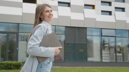 A girl in a business suit with a laptop in her hands walks down the street against the backdrop of a monumental building. Business. Attractive business girl. Career people. Look at the camera