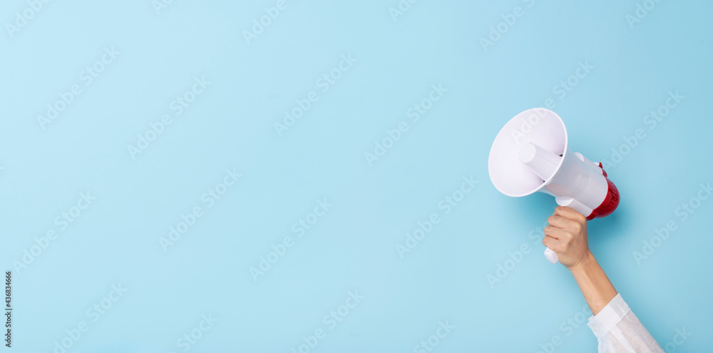 Business Hand holds a megaphone from a hole in the wall on blue background.  hiring, advertising, advertise and Banner concept. - obrazy, fototapety, plakaty 