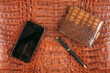 Phone, wallet and pen lying on brown crocodile skin. Business
