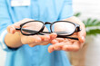 Woman doctor optometrist in blue uniform holds in her hands and gives a pair of glasses to a patient in a clinic or optical store. Ophthalmology, vision correction and protection, eye health concept