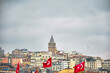© SKahraman - 03.03.2021. istanbul Turkey. Galata Tower in istanbul during overcast sky and rainy day. Photo from eminonu district with many turkish flag waving by wind hanging on fish and chips sellers boats and s