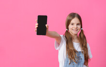 Girl Of 10 Years Old In A White Top Holds A Black Phone On A Pink Background