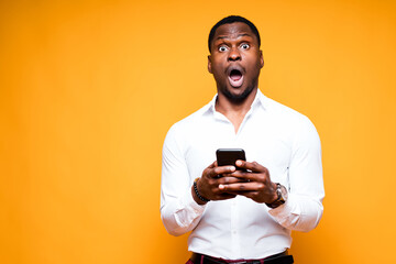 Handsome african american businessman holding a phone in his hands and looking at the camera surprised