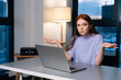 © dikushin - Frustrated young woman confused by laptop computer problem sitting at desk in home office near window evening at late, looking at camera. Bewildered female spreads hands incomprehensibly.