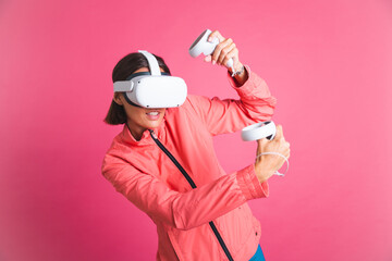 Young fit woman in sport wear jacket and virtual reality glasses playing boxing fight games on pink background