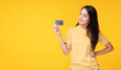 © kaew6566 - Payment purchase and financial concept. Cheerful young woman wearing casual clothes while holding and looking at credit card mockup in own hand while standing over isolated yellow background.