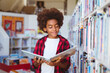 © WavebreakMediaMicro - Smiling african american schoolboy reading book standing in school library