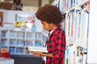 © WavebreakMediaMicro - Happy african american schoolboy reading book standing in school library