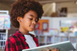 © WavebreakMediaMicro - Smiling african american schoolboy reading book standing in school library