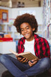 © WavebreakMediaMicro - Portrait of smiling african american schoolboy reading book sitting on floor in school library