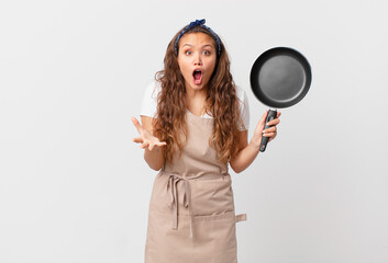 Wall Mural - young pretty woman feeling extremely shocked and surprised chef concept and holding a pan