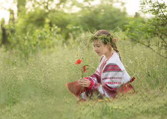 Wall Mural - A girl in a Belarusian folk costume sits in the forest with a wreath on her head and flowers in her hands. The concept of the traditions of the Slavic people.