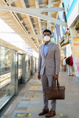 Wall Mural - African businessman at train station platform wearing face mask while waiting train