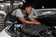 © Roman - african woman under the hood of white car. woman in uniform mechanic repairing a car in car service. portrait of young black female enjoying work with automobile, vehicle