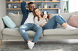 © Prostock-studio - Cheerful multicultural spouses relaxing on couch with smartphone together